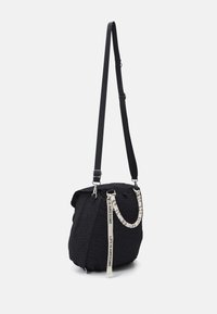 Czarna pikowana torba crossbody z regulowanym paskiem, wyróżniająca się teksturowaną powierzchnią oraz kontrastującą wzorzystą rączką z nadrukowanym tekstem. Szczegóły z zamkiem błyskawicznym.