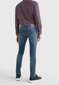 Blå denim skinny jeans med fram- och bakfickor, kombinerat med en mönstrad mörk skjorta som visar sömnadsdetaljer och en läderetikett.