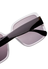 Mustat ja valkoiset aurinkolasit, joissa on leveä kehys ja liukuväriset purppurat linssit. Sangen ovat mustat ja kiiltävät, ja niissä on pieni kaarevuus sekä pieni yksityiskohta.