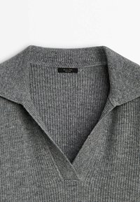 Pull en maille côtelée gris avec col rabattu et décolleté en V, mettant en avant la texture et le détail du tissu.