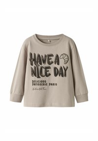 Lichtbeige langekoe T-shirt van katoen; heeft zwarte tekst: "GENIET VAN JE DAG" en "LEKKERE PATISSERIE PARIJS" met een croissantafbeelding.