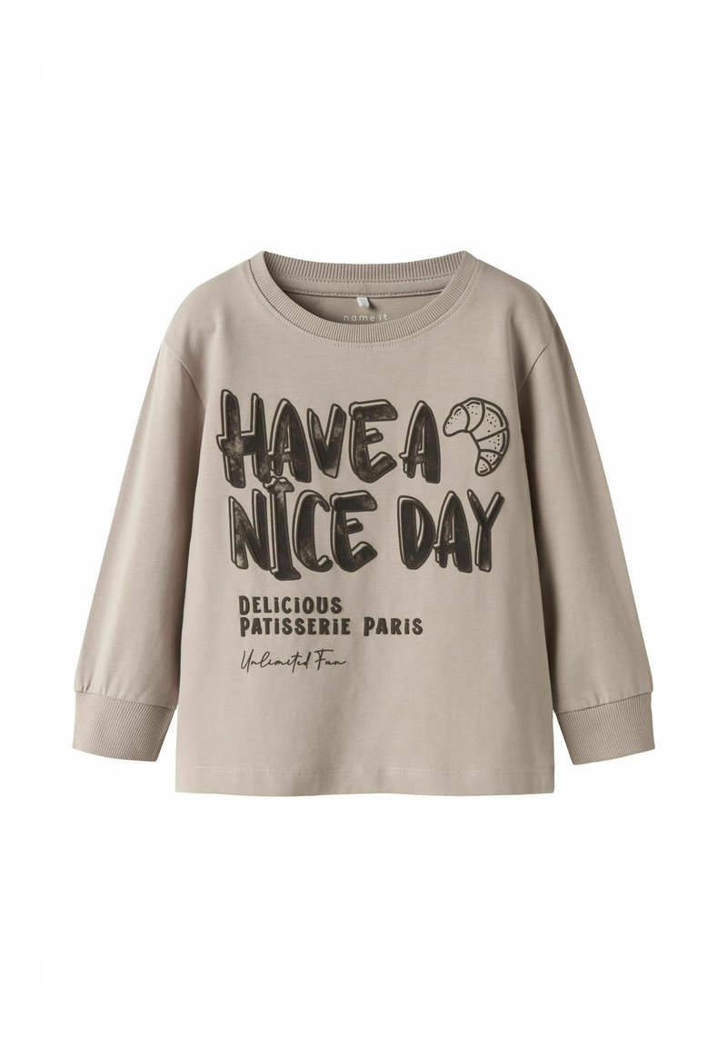 Lichtbeige langekoe T-shirt van katoen; heeft zwarte tekst: "GENIET VAN JE DAG" en "LEKKERE PATISSERIE PARIJS" met een croissantafbeelding.