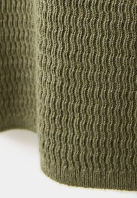 Gros plan d’un tissu tricoté vert olive avec un motif côtelé texturé et des fibres douces visibles.