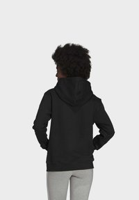 Felpa nera con tasca a marsupio, lacci regolabili e polsini a costine. Indossata con pantaloni sportivi grigi, per un look casual.