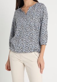 Leopardenmusterbluse in Hellblau und Schwarz, mit V-Ausschnitt und Dreiviertelärmeln, aus weichem, leichtem Stoff.