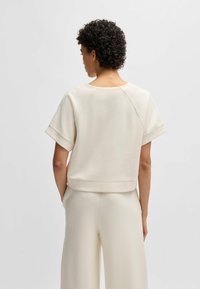 Cream-colored sweatshirt, soft texture, short sleeves, round neckline, and relaxed fit, shown from the back with visible seam detailing.