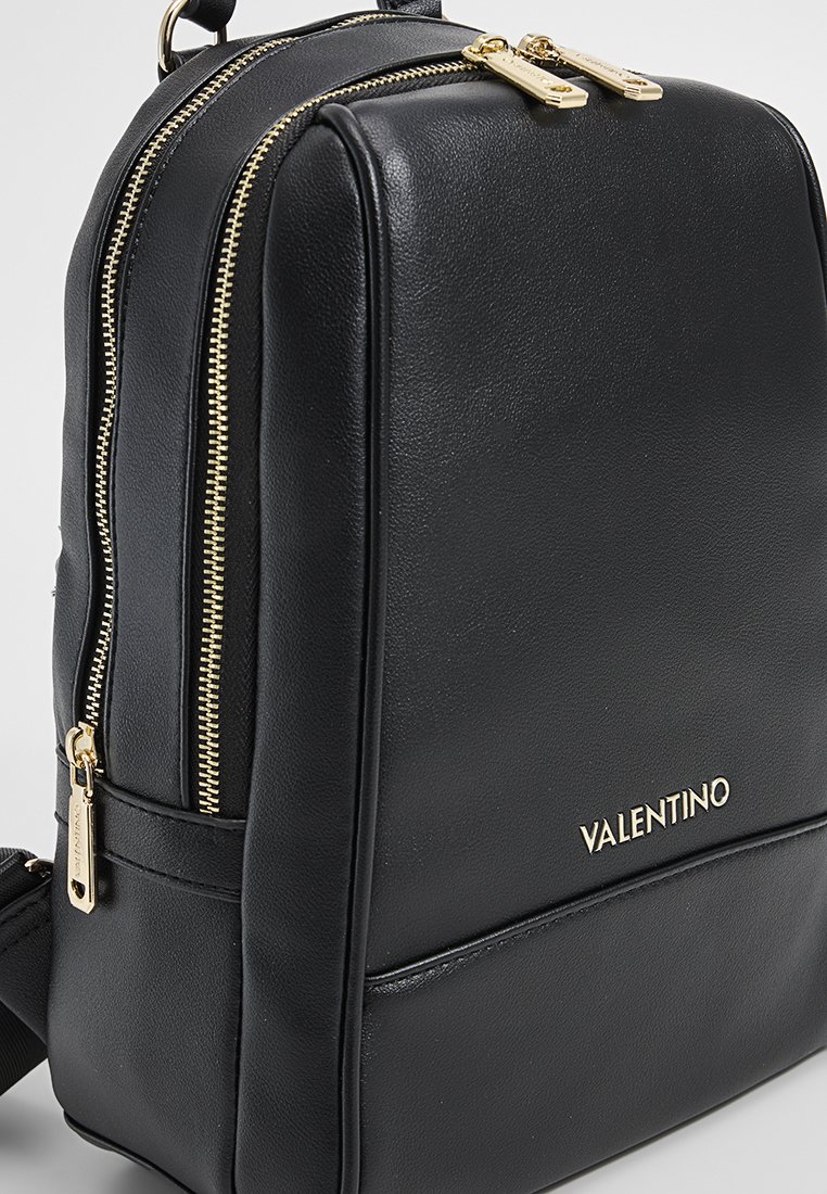 Schwarzer Leder-Rucksack mit goldenen Reißverschlüssen, glatter Oberfläche, rechteckiger Form und einem Logo-Detail auf der Vorderseite. Zwei Fächer zur Aufbewahrung.