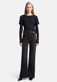 Zwart T-shirt met korte mouwen over een top met lange mouwen, gecombineerd met donkere uitlopende jeans en een zwarte leren riem. Strakke zwarte enkellaarzen.