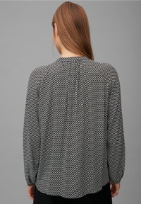 Svart- och vitmönstrad långärmad blus med en samlad halsringning och plisseringar på baksidan. Lätt tyg med en slät textur.