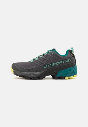 Trail running shoe with a black mesh upper, turquoise accents, green laces, and a rugged rubber outsole with yellow traction studs.