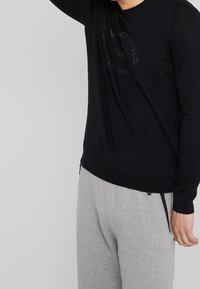 Svart långärmad tröja med präglad logotyp. Ribbad mudd och midja. Bärs med ljusgrå sweatpants med sidonesfickor.