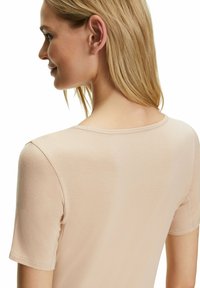 Korte mouw, aangesloten top van lichtbeige stof. Beschikt over een ronde halslijn en een gladde textuur met nette naden op de schouders en achterkant.