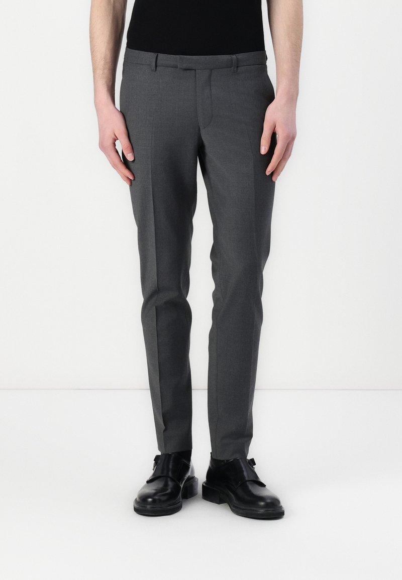 Szürke, sima textrű, slim fit szabású nadrág, övbújtatókkal, fekete cipőkkel párosítva. Az anyaga könnyűnek és struktúrált kinézetűnek tűnik.