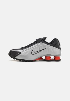 Chaussure de course Nike noire et argent avec trois amortisseurs rouges en forme de ressort sur la semelle et des lacets noirs.