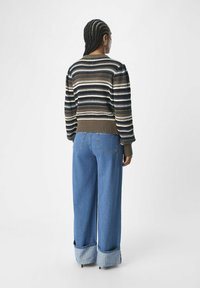 Sweter z prążkowanego dzianiny w ziemistych odcieniach, z prążkowanym dołem, w zestawieniu z szerokimi niebieskimi dżinsami z zawiniętymi nogawkami i dwoma tylnymi kieszeniami.
