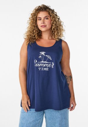 Žena s kučeravými vlasmi nosi tmavomodré tielko s nápisom „Summer Time“ a dizajnom palmy, v páre s svetlomodrými pruhovanými nohavicami.