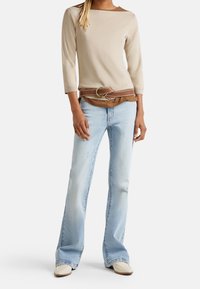 Beige långärmad topp, brun bälte med cirkulär accent, ljusblå utsvängda jeans och off-white skor. Strukturerad tyg med enfärgade nyanser.