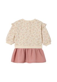 Cremfarbene Bluse mit langen Ärmeln und Rüschendetails, kombiniert mit einem pinken Strickrock, der einen Rückenschlitz mit Knopfverschluss hat.