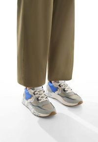 Sneaker sportive grigie e blu con tessuto texturizzato, lacci bianchi e suole spesse con accenti beige e dettaglio del logo sul lato.