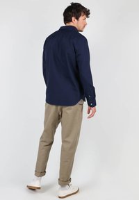 Chemise à manches longues marine, en mélange de coton, avec des poignets à boutons ; associée à un pantalon beige fuselé, à ourlets retroussés, et des baskets blanches avec des semelles brunes.