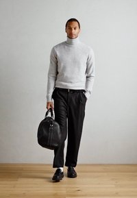 Pull en col roulé gris, pantalon noir ajusté, sac en cuir noir avec poignées et chaussures noires sur un sol en bois contre un mur neutre.