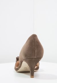 Chaussure à talon haut en suède marron pour femmes, vue de dos, avec un talon pointu et une pointe arrondie sur une surface blanche.