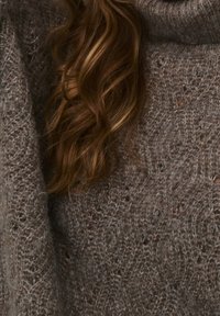 Brązowy dziergany sweter o strukturalnym wzorze i luźnym golfie. Materiał wydaje się miękki i puszysty, zapewniając ciepłe, przytulne uczucie.