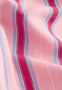 Tuva auduma tuvplāns ar rozā, violetām, sarkanām un baltām vertikālām svītrām un strukturētu austumu, kurā redzamas maigas locījumi un ēnas.