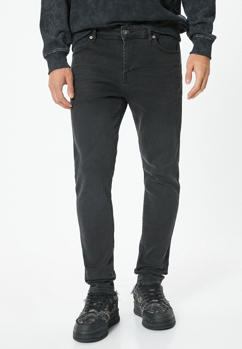 Jeans de mezclilla negra con corte slim, con una cintura de altura media, diseño de cinco bolsillos y una sutil textura desgastada. Combinados con zapatillas negras.