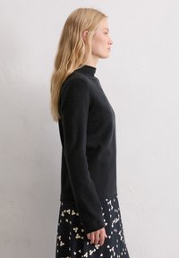 Schwarzer Rollkragenpullover aus weichem Stoff mit langen Ärmeln und geradem Schnitt. Kombiniert mit einem marineblauen Rock mit floralem Muster.