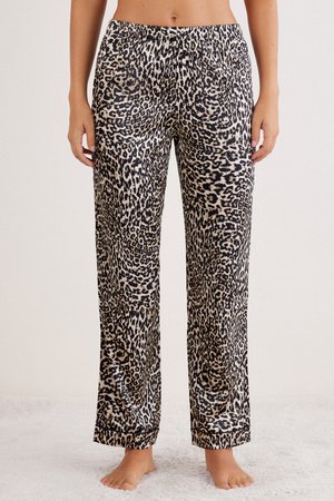 Femme portant un pantalon ample à imprimé léopard avec taille élastique, debout pieds nus sur un tapis clair devant un fond uni.