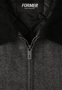 Chaqueta gris de espiga con cuello de pana negro, cremallera frontal y herrajes metálicos que presentan el logo "FF". Interior forrado.