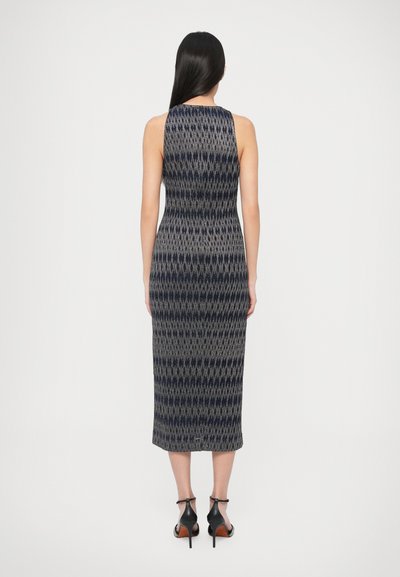 Megzta midi suknelė su geometriniu raštu tamsiai mėlynos ir pilkos spalvų tonais, be rankovių, prigludusiu siluetu. Juodi aukštakulniai bateliai.