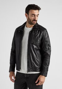 Svart läderjacka med dragkedja, axelaccenter och räfflad textur på axlarna. Bärs över en ljusgrå tröja.