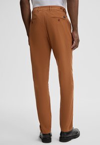 Braune Baumwollhosen mit geradem Bein, ausgestattet mit einem Knopfverschluss am Bund, hinteren Taschen und einer glatten Textur.