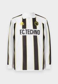 Langermet fotballdrakt i hvite og svarte vertikale striper, med gule detaljer, krage, logo og "F.C.TECHNO" -bokstaver.