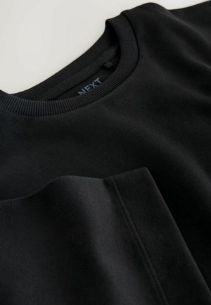 Svart sweatshirt med rund halsringning, ribbade muddar och en slät textur. Har en diskret bröstficka. Märkning synlig på insidan av kragen.