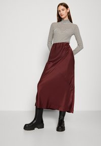 Fustă maxi din satin burgundy, asortată cu un pulover cu gât în dungi negre și albe, completată cu cizme cu platformă negre până la genunchi.