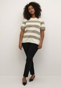Tricou cu dungi în culori deschise, cu mâneci scurte tip puff, având dungi bej și crem, combinat cu pantaloni negri ajustați și mocasini negri.