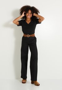 Top negro de cuello en V con mangas de encaje, combinado con pantalones anchos negros. Accesorios con un cinturón marrón y sandalias de tacón grueso.