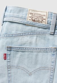 Poche arrière de jean en denim bleu clair avec étiquette rouge Levi's et une étiquette de marque en cuir cousue à la ceinture.