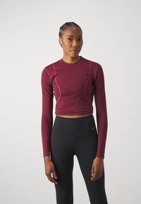 Bordo ilga rankovė crop top'as su kontrastingomis rožinėmis siūlėmis, prigludusi siluetas ir apvalia iškirpte, derinamas su aukštai juosmeniu juodais legginais.