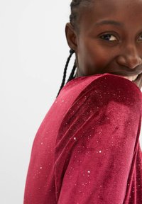 Top in velluto cremisi con paillettes scintillanti, scollatura rotonda e spalle drappeggiate, caratterizzato da una texture liscia e una silhouette aderente.