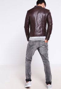 Brun läderjacka med skräddarsydd passform, med ståkrage och dragkedjeärmar, i kombination med grå denimjeans och vita sneakers.