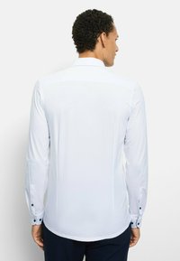 Weißes Langarmhemd mit glatter Textur, schmalen Manschetten mit dunkelblauen Knöpfen und klassischem Kragen. Nur Rückansicht.