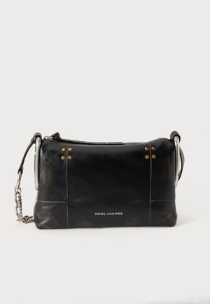 Μαύρη δερμάτινη τσάντα Marc Jacobs με ασημένιο ιμάντα αλυσίδας και χρυσά καρφιά σε απλό ανοιχτό φόντο.