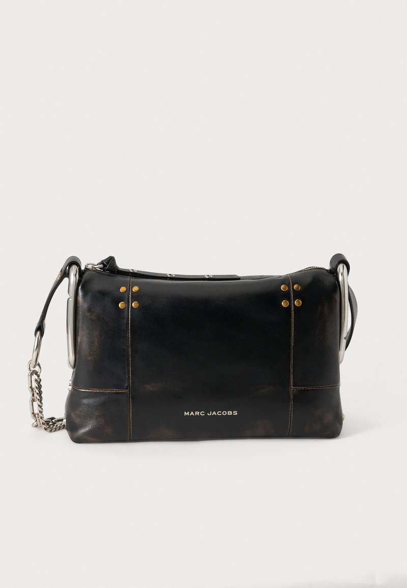 Μαύρη δερμάτινη τσάντα Marc Jacobs με ασημένιο ιμάντα αλυσίδας και χρυσά καρφιά σε απλό ανοιχτό φόντο.