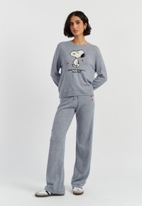 Grijs loungewearset met een sweatshirt met een Snoopy-graphic en de tekst "Peanuts origineel sinds 1950", vergezeld van bijpassende broeken.