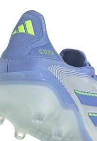 Blue soccer cleat featuring a textured upper, neon green accents, and a transparent sole with multiple studs for traction. "COPA" logo present.