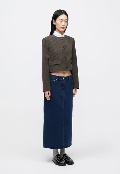 Barna tűsarkú felhajtható blézer két zsebbel, hosszú kék farmer szoknyával és fekete bebújós cipővel, szürke zoknival párosítva.